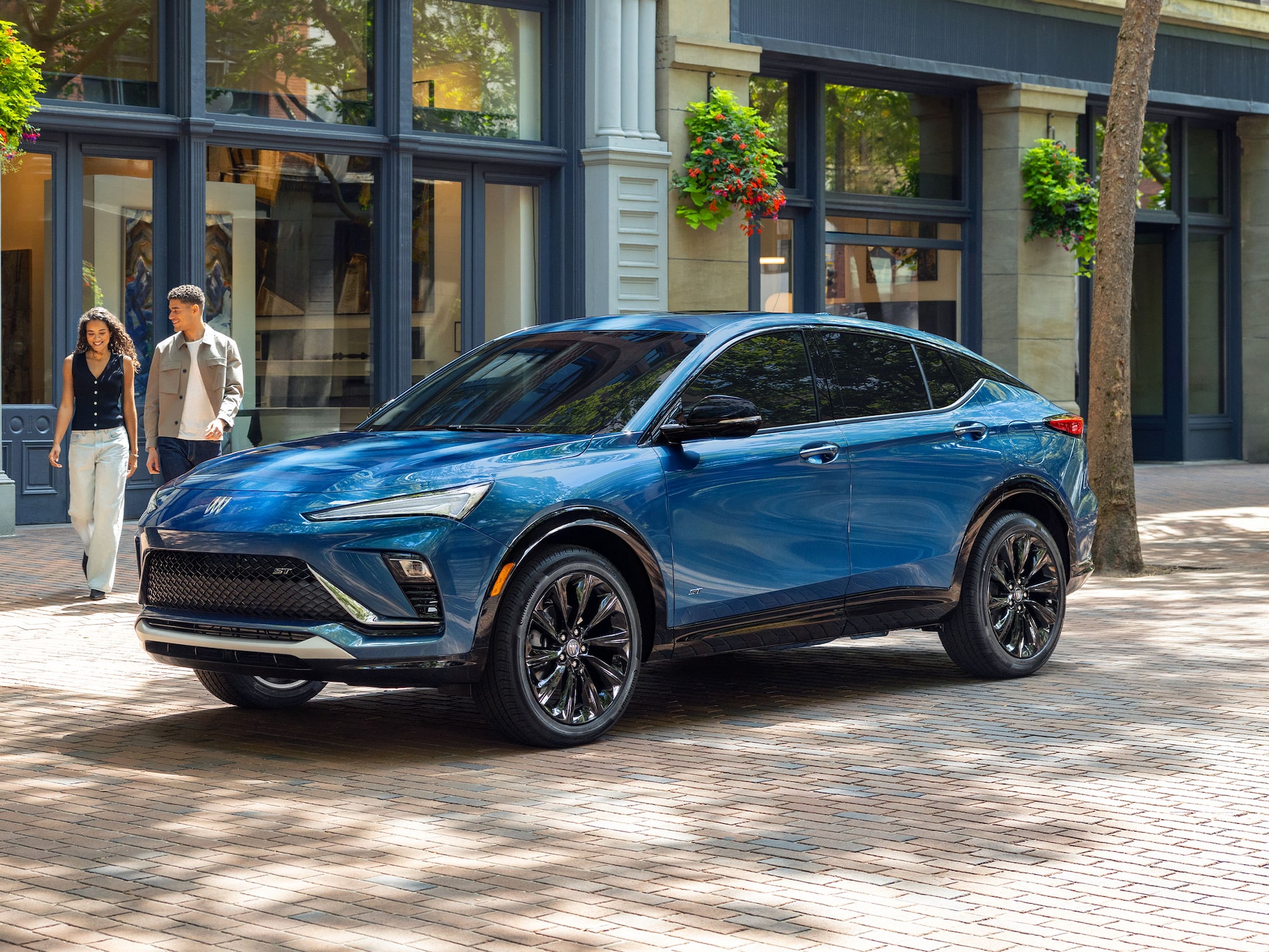  A Brilliant Blue Buick Envista ST SUV Parked on a Brick Sidewalk as Two People Walk Past a Storefront in the Background