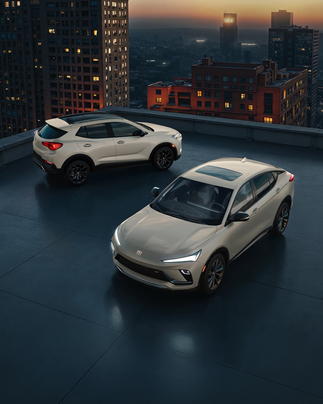 Front View of the 2026 Envista ST SUV and the 2026 Encore GX ST SUV both in the Color Ceramic, Parked on a City Rooftop