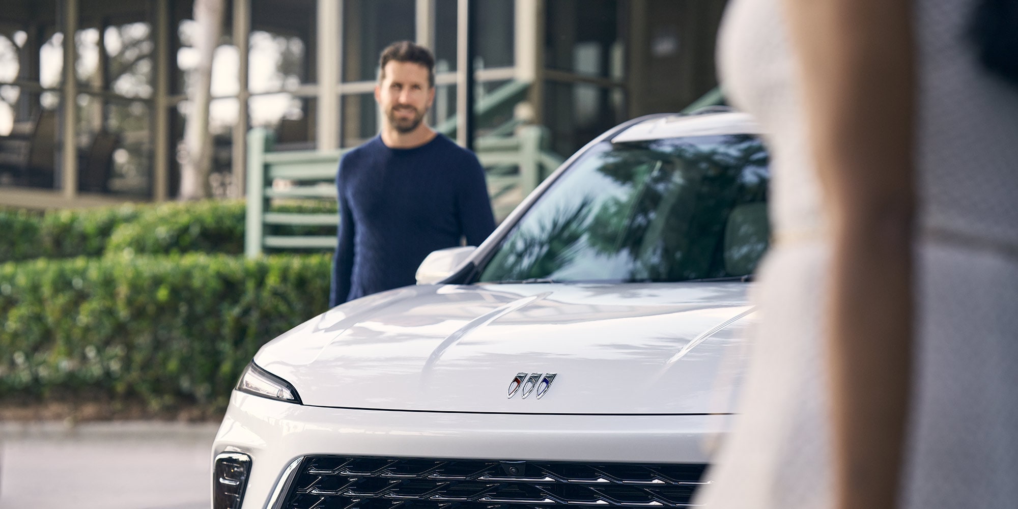 A Smiling Man Stands Near a White Buick SUV Showing the Brand Logo on Its Hood