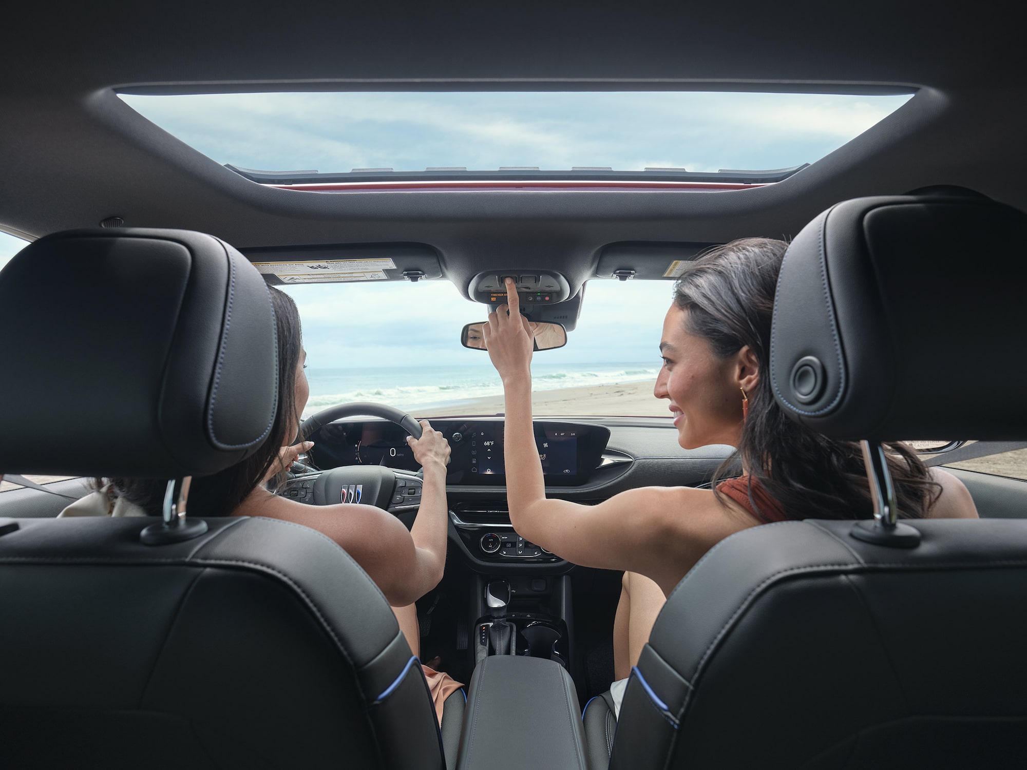 Two Women Drive a Buick Along the Ocean One Steers with the Buick Logo and the Other Adjusts the Overhead Console
