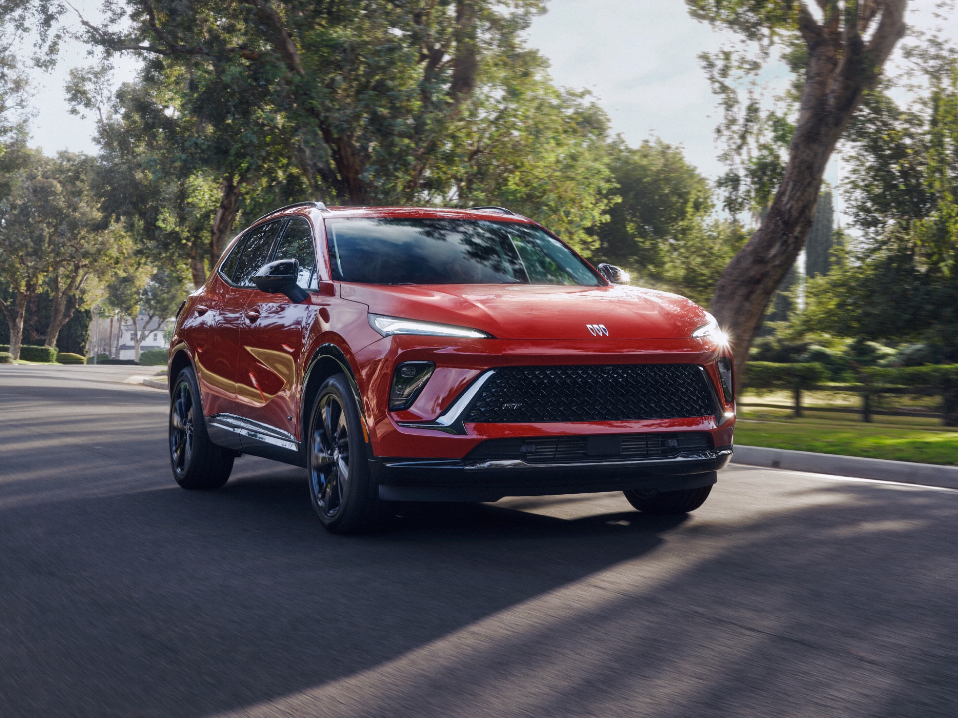 A Striking Red Buick Envista ST Driving Towards the Viewer on a Sunny Road Lined with Green Trees