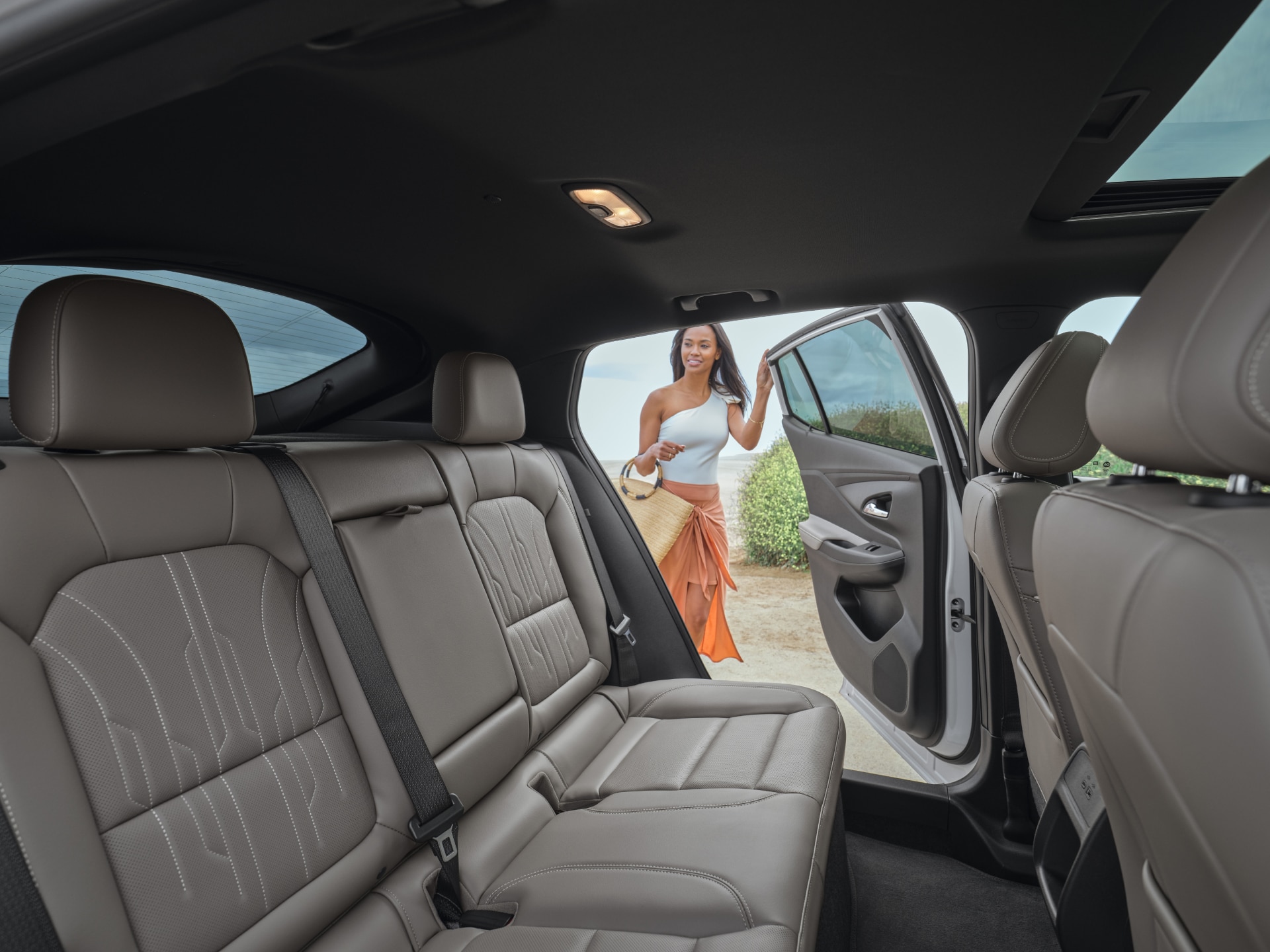 View from Inside a White Buick SUV Showing the Rear Gray Leather Seats with a Woman in an Orange Skirt and White Top Getting into the Driver’s Side