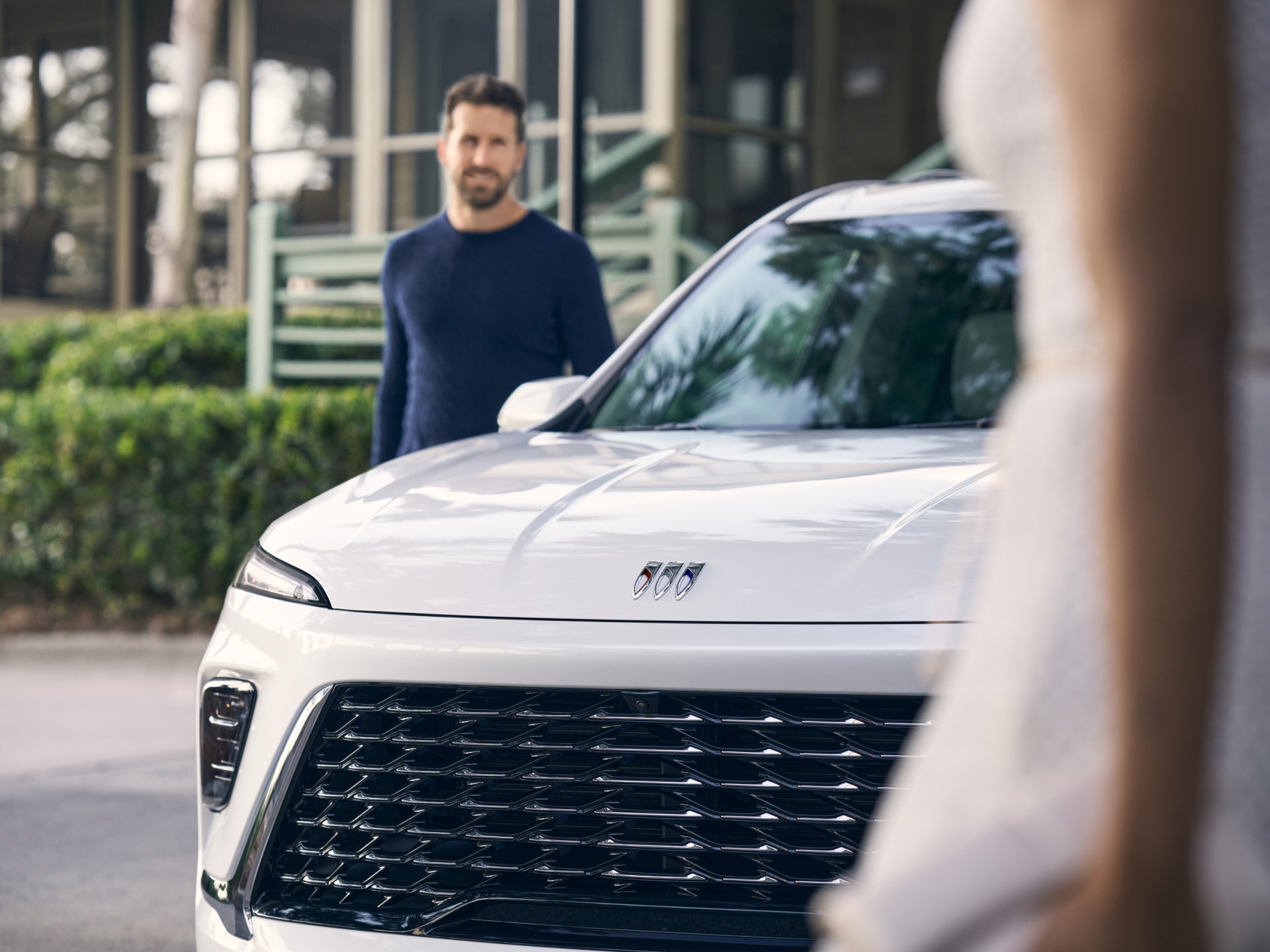 A Smiling Man Stands Near a White Buick SUV Showing the Brand Logo on Its Hood