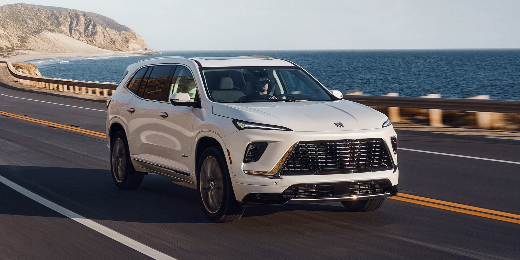 A White Buick Enclave Driving Along a Coastal Road with the Ocean and Cliffs in the Background