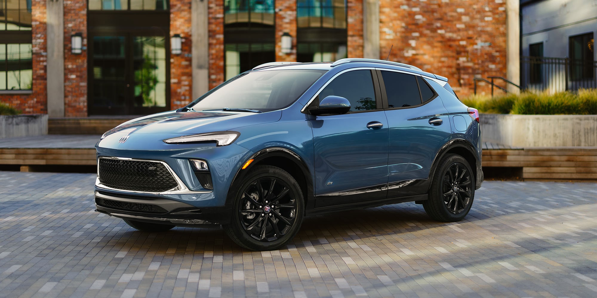 A Metallic Blue Buick Encore GX Parked on a Patterned Brick Walkway in Front of an Old Brick Building with Large Windows
