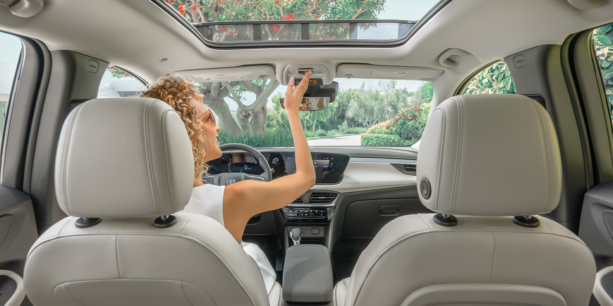 A Person in the Passenger Seat of a Buick SUV Adjusting the Rearview Mirror, with a Panoramic Sunroof Visible