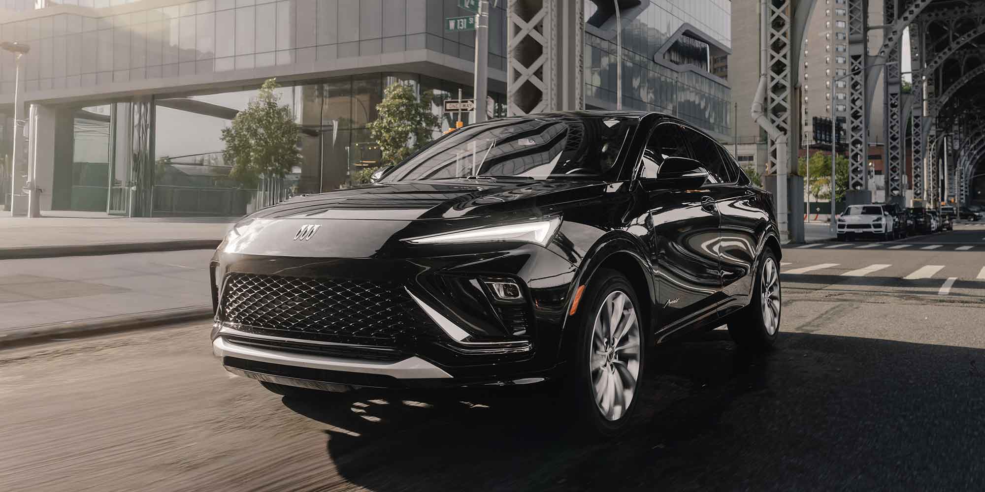 A Black Buick Envista Driving on a City Street with Modern Buildings and a Bridge Structure in the Background