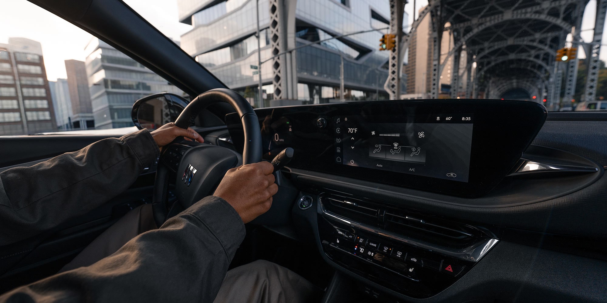 A Person's Hands on the Steering Wheel of a Buick Vehicle, Showing the Driver's Perspective of a City Street and a Digital Dashboard