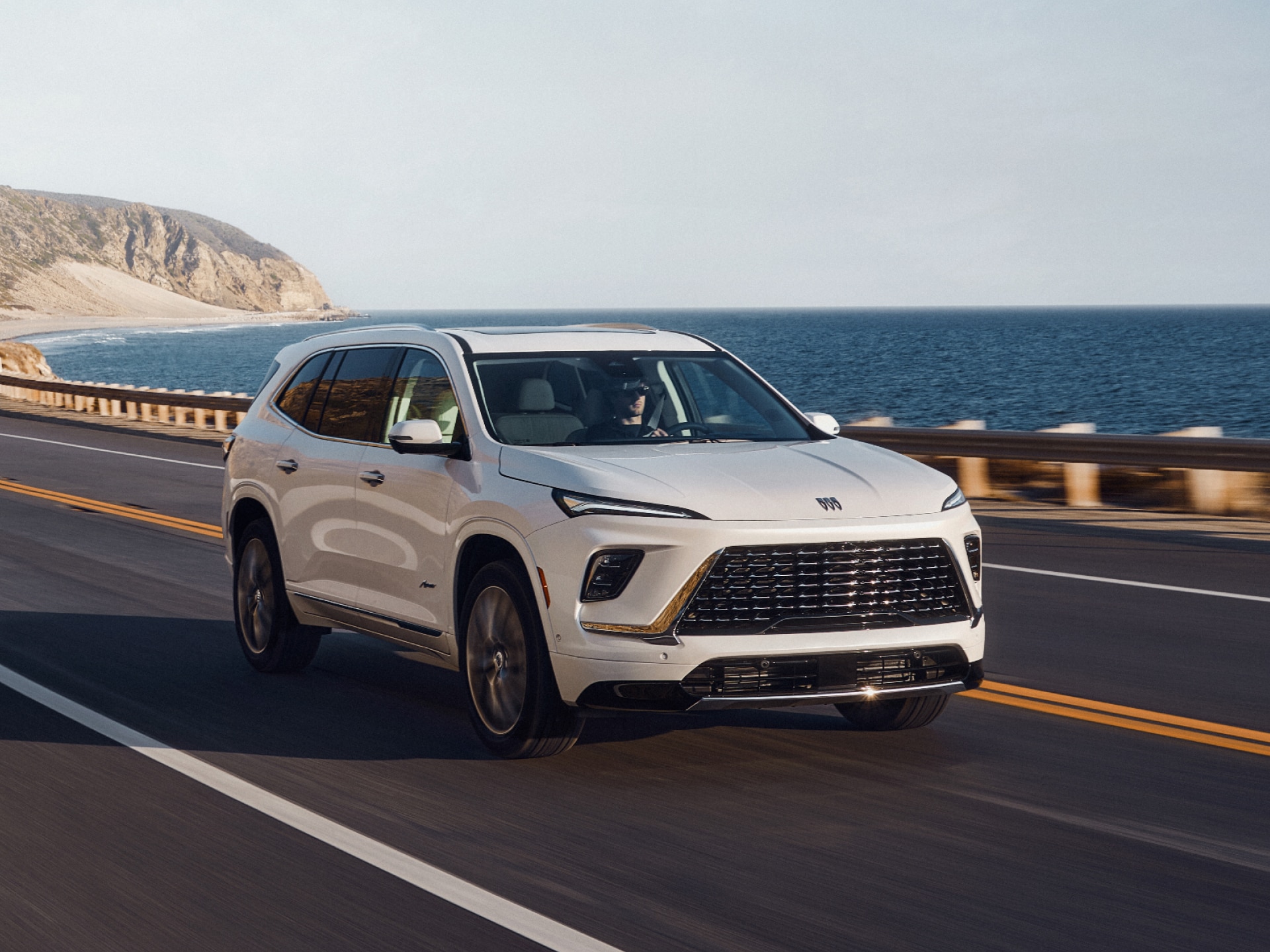 A White Buick Enclave Driving Along a Coastal Road with the Ocean and Cliffs in the Background
