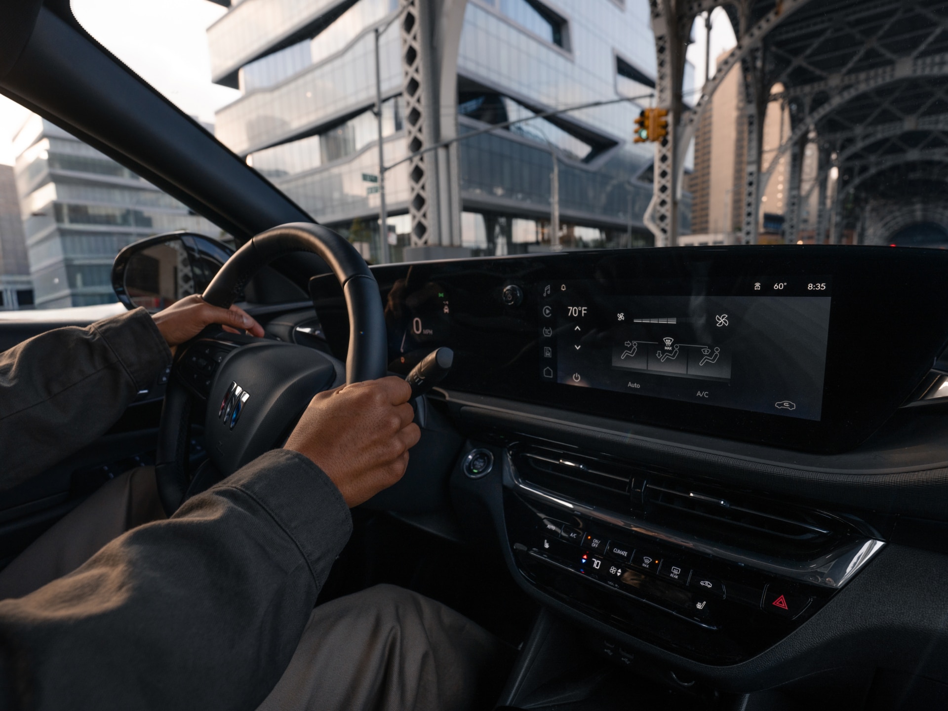 A Person's Hands on the Steering Wheel of a Buick Vehicle, Showing the Driver's Perspective of a City Street and a Digital Dashboard