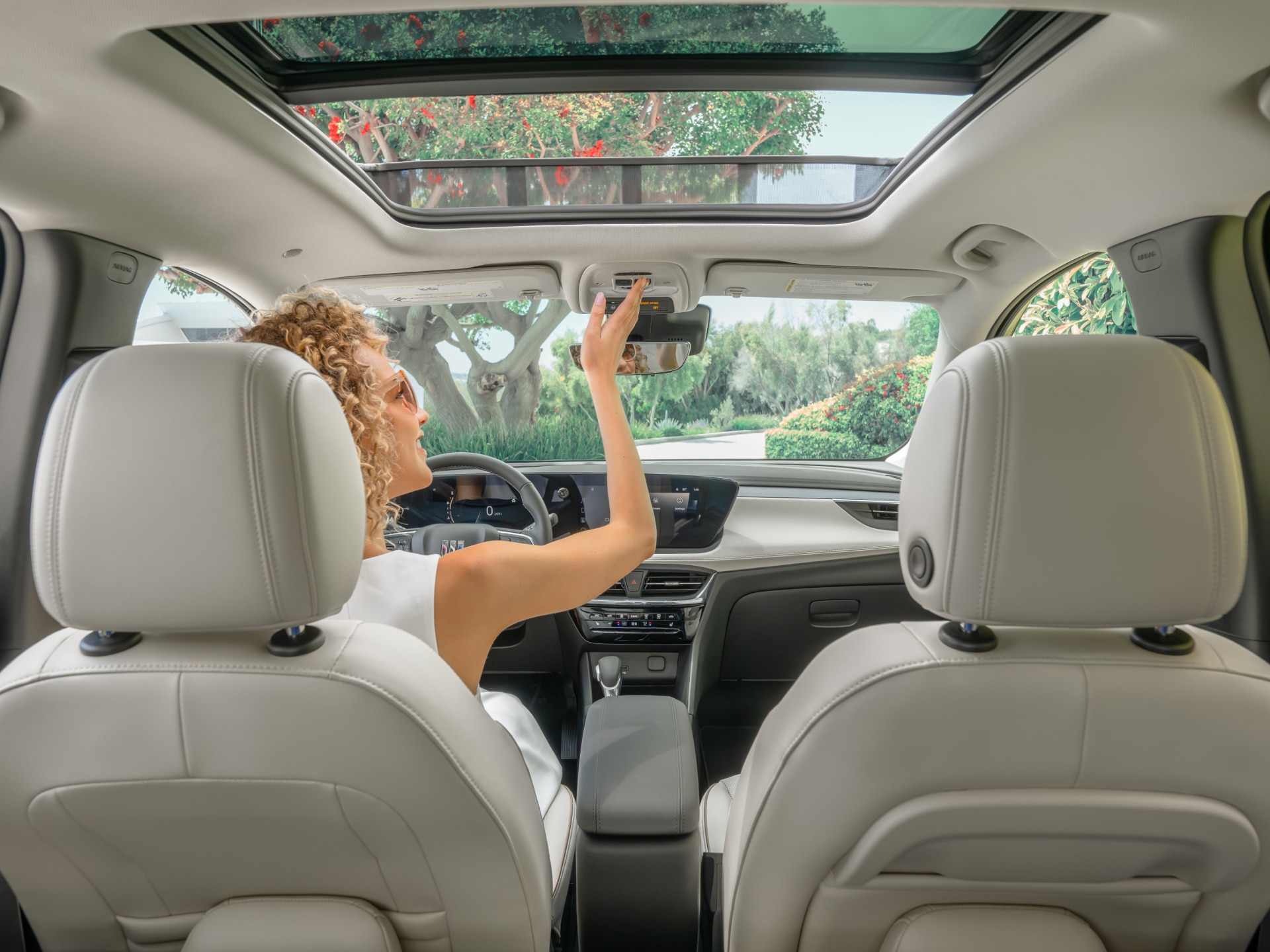 A Person in the Driver Seat of a Buick SUV Adjusting the Rearview Mirror, with a Panoramic Sunroof Visible