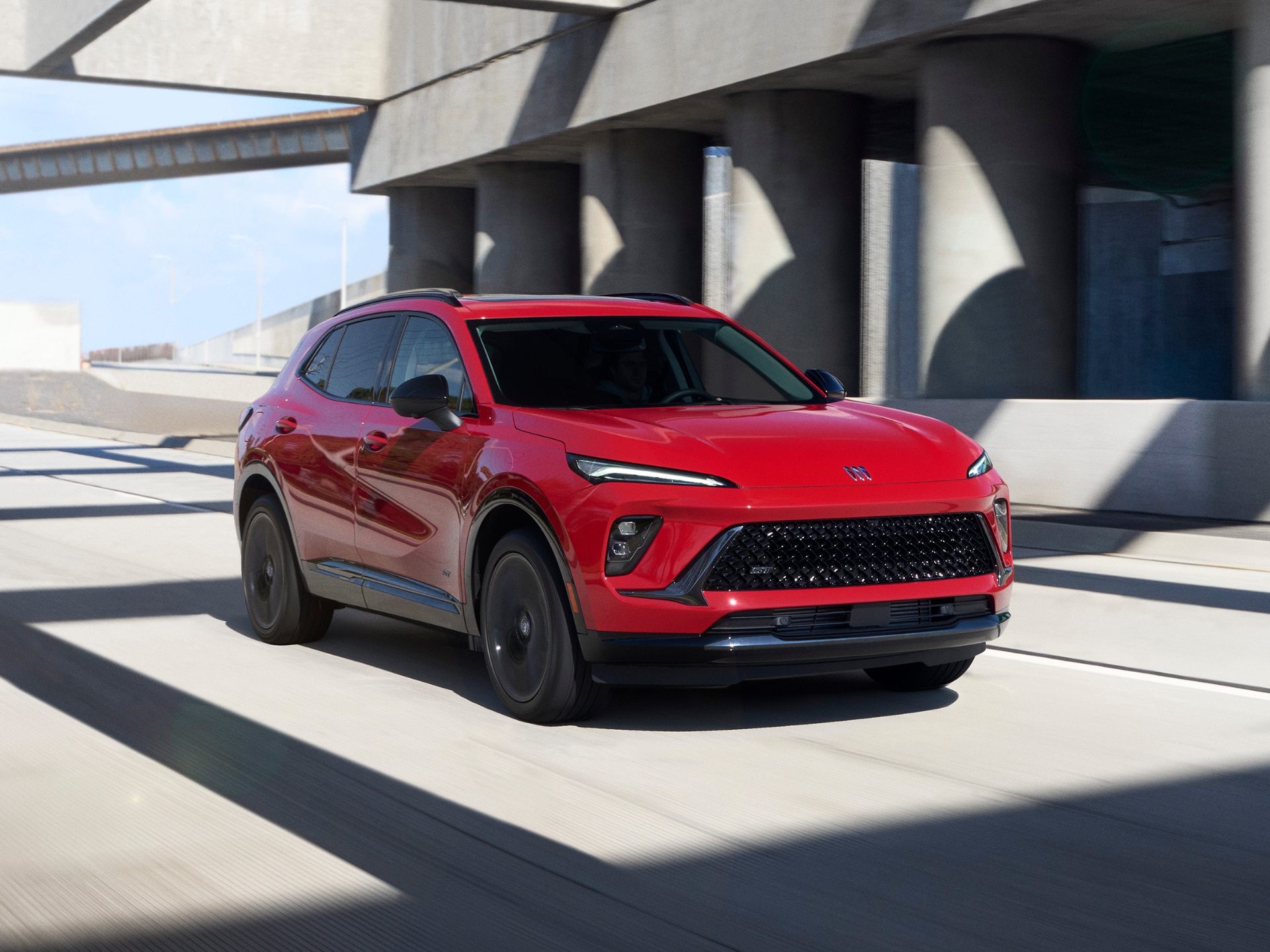 A Red Buick Envision Driving on a Road under an Overpass with Modern Architecture in the Background