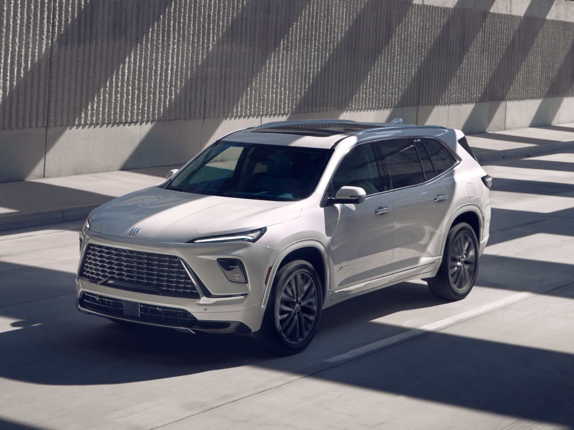 A Front Three-Quarters View of a White Buick Enclave Avenir Driving Along a Shadowy Street