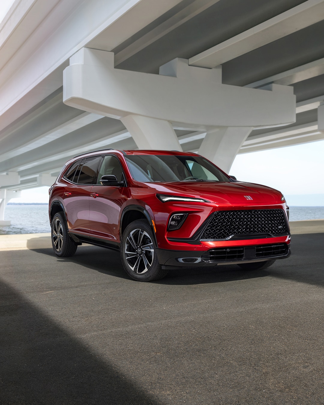 A Front Three-Quarters View of a Red Buick Enclave ST Parked Beneath a White Bridge Near the Ocean