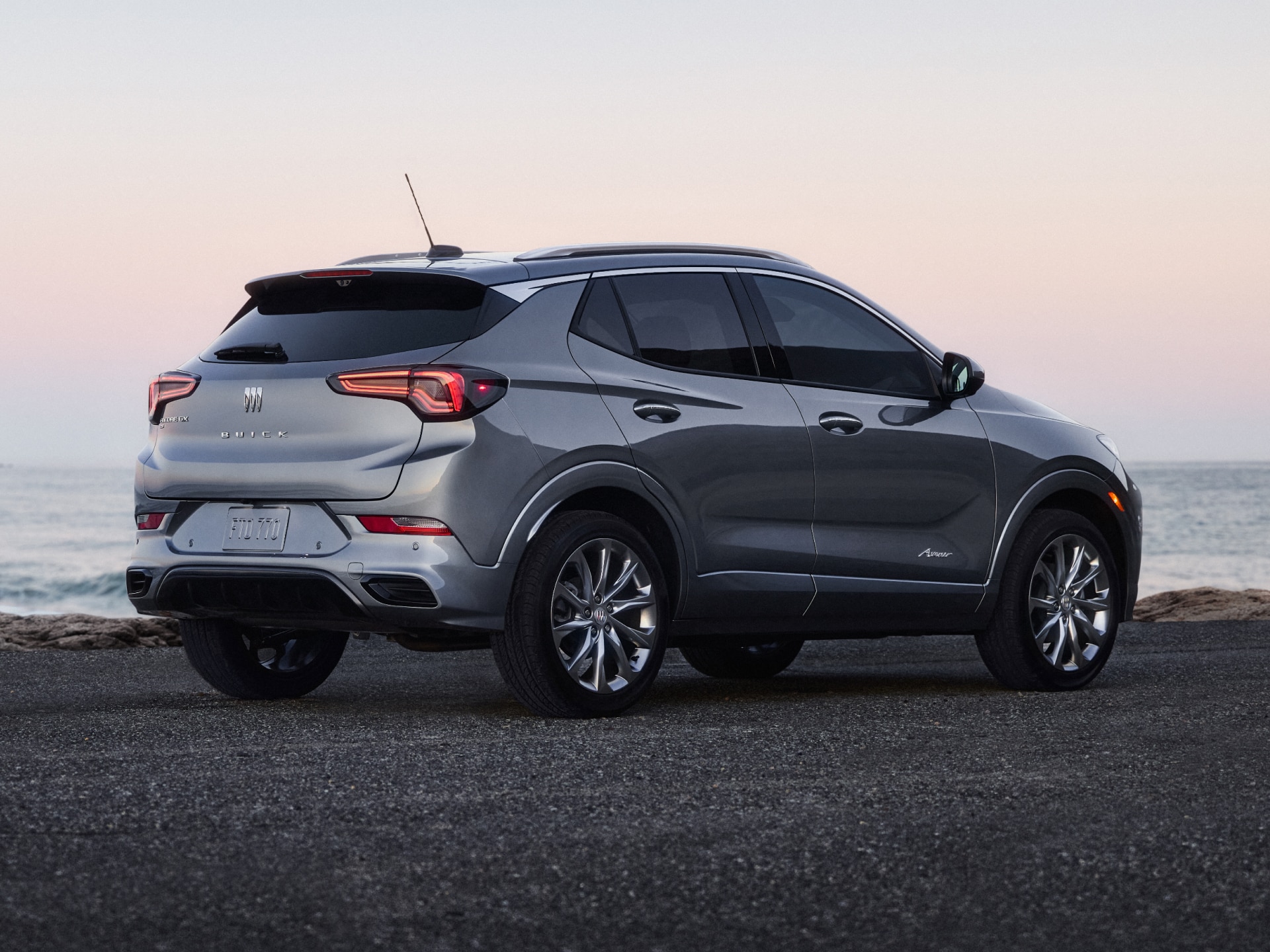A Rear Three-Quarters View of a Silver Buick Encore GX Avenir Parked on a Beach at Sunset