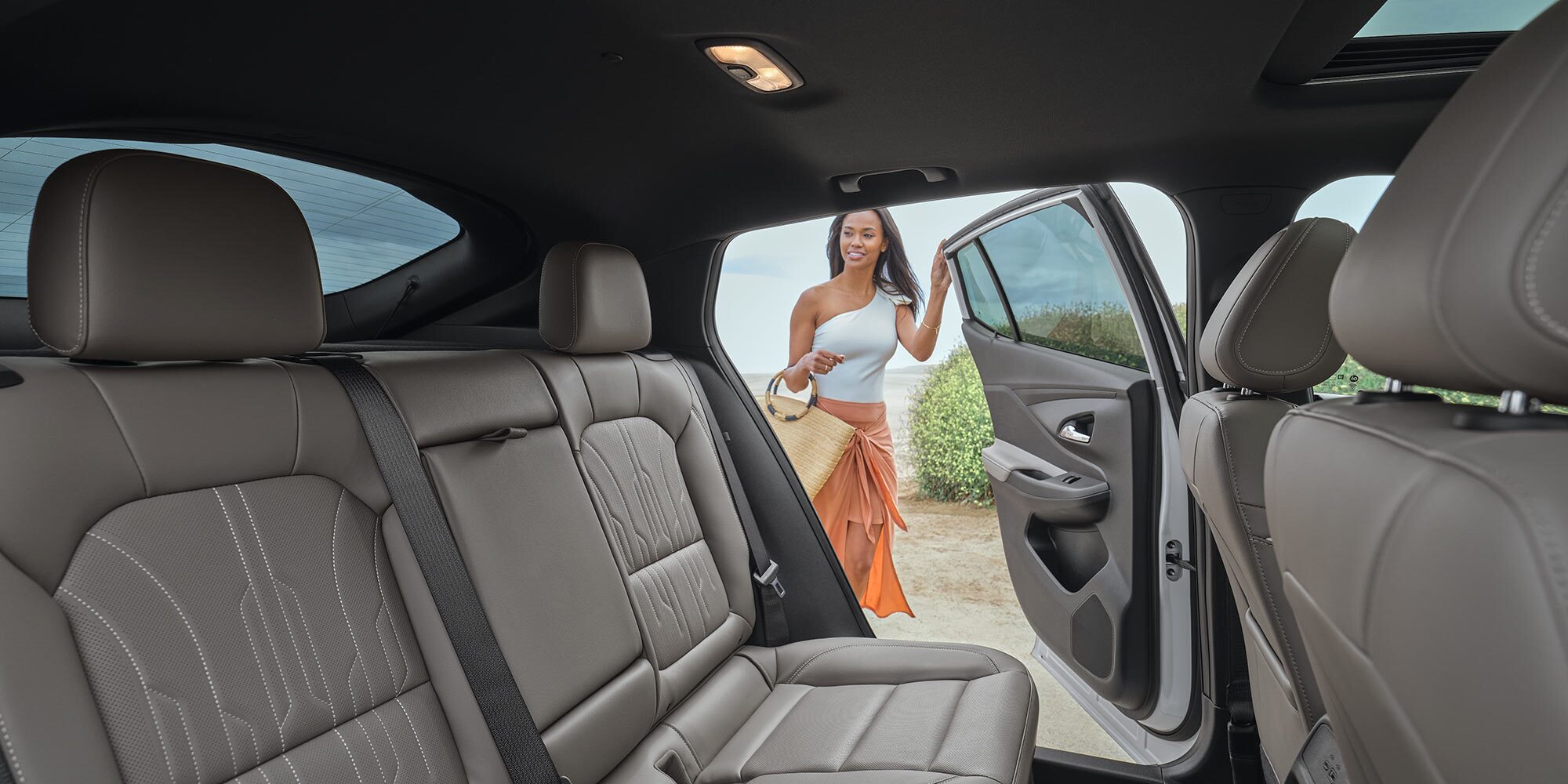 View from Inside a White Buick SUV Showing the Rear Gray Leather Seats with a Woman in an Orange Skirt and White Top Getting into the Driver’s Side