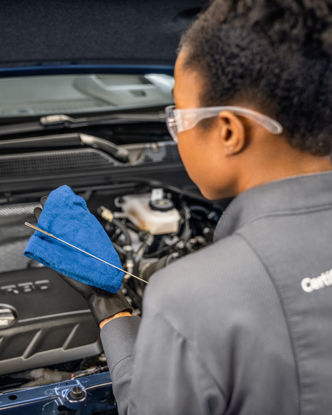 A Technician in Safety Glasses Checks the Oil in a Buick Engine with a Blue Cloth and Dipstick
