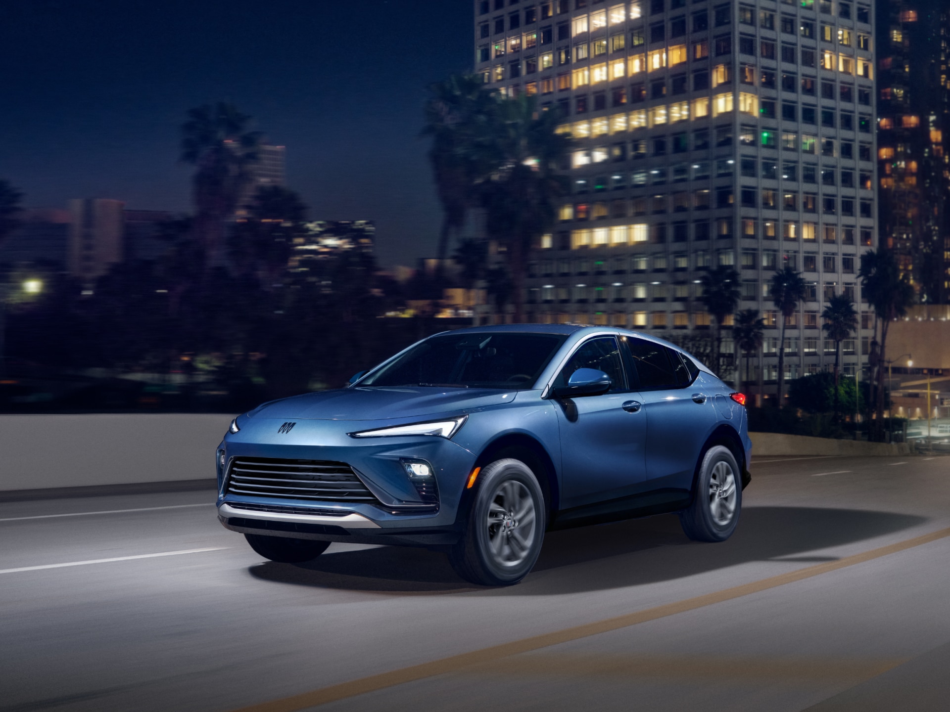A Blue Buick SUV Drives on a City Street at Night with Illuminated Buildings in the Background