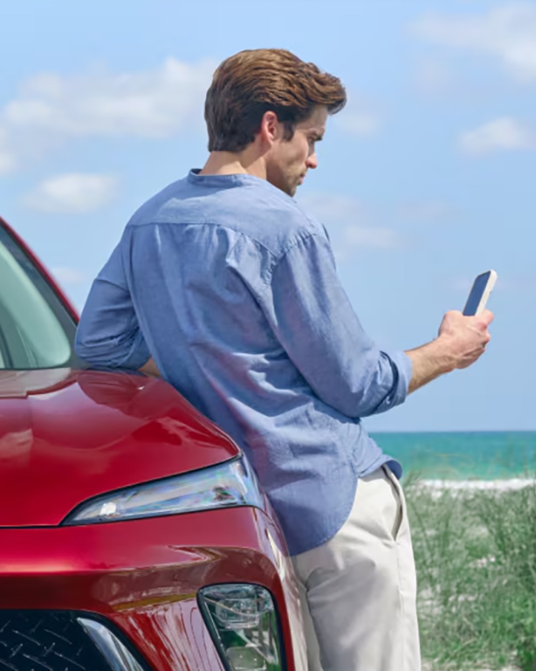 A Man Leaning on the Hood of His Buick Vehicle Using His Smartphone
