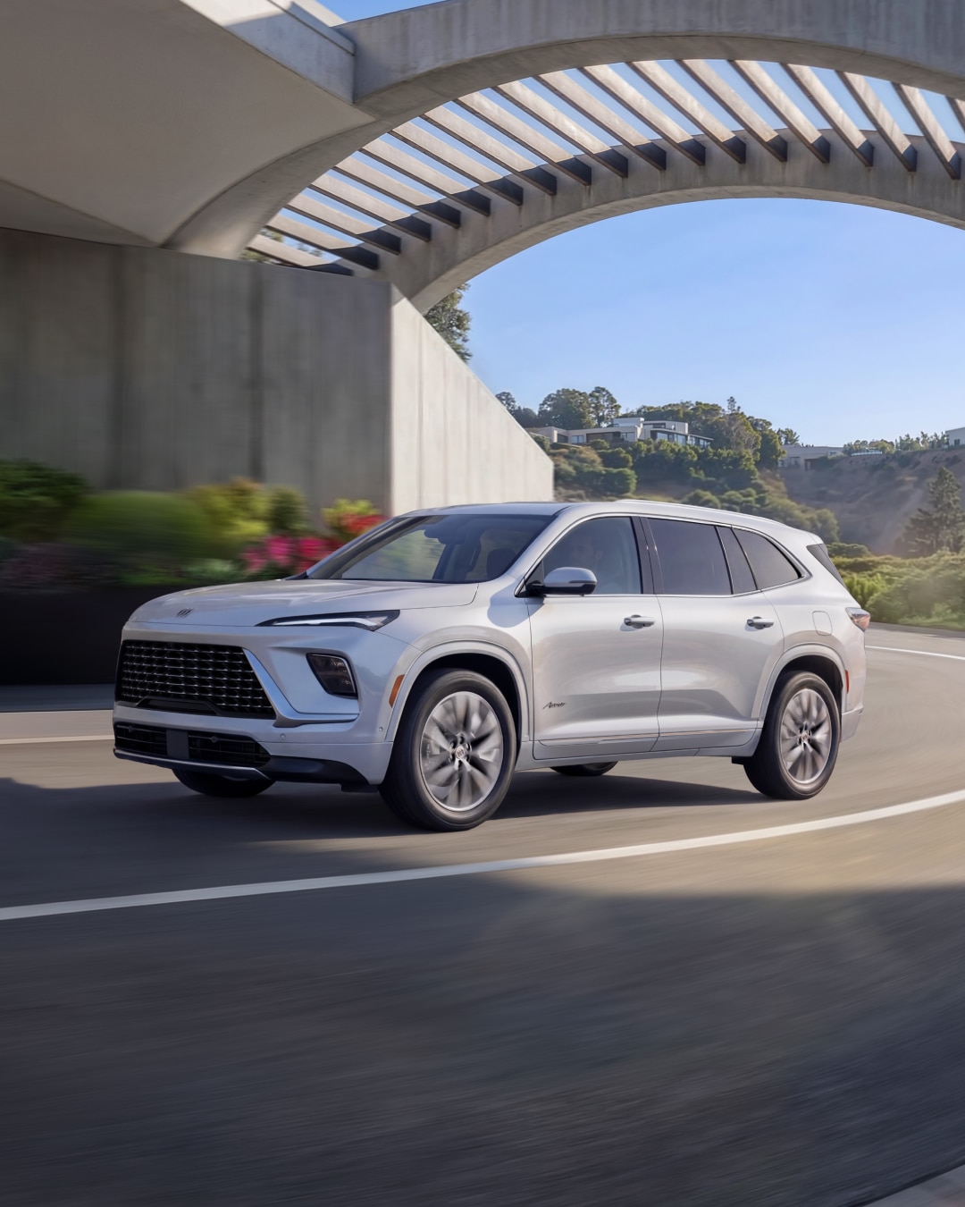 A White Buick SUV Driving on a Winding Road Under a Modern Concrete Archway