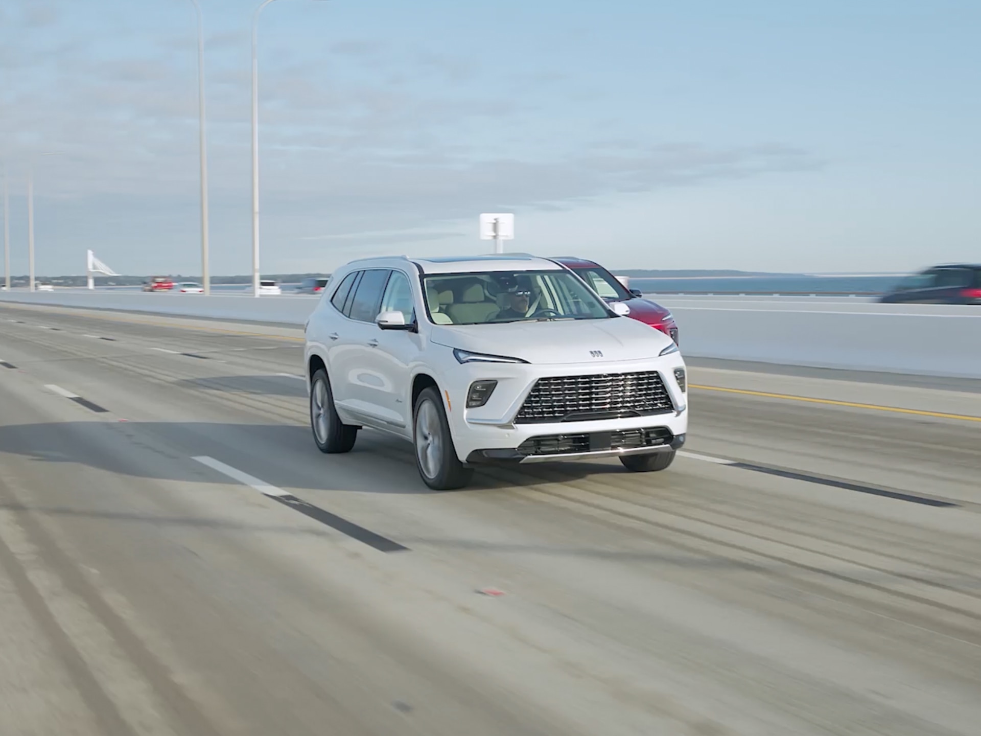 A Silver Buick SUV Drives Across a Multi Lane Bridge Under a Partly Cloudy Sky