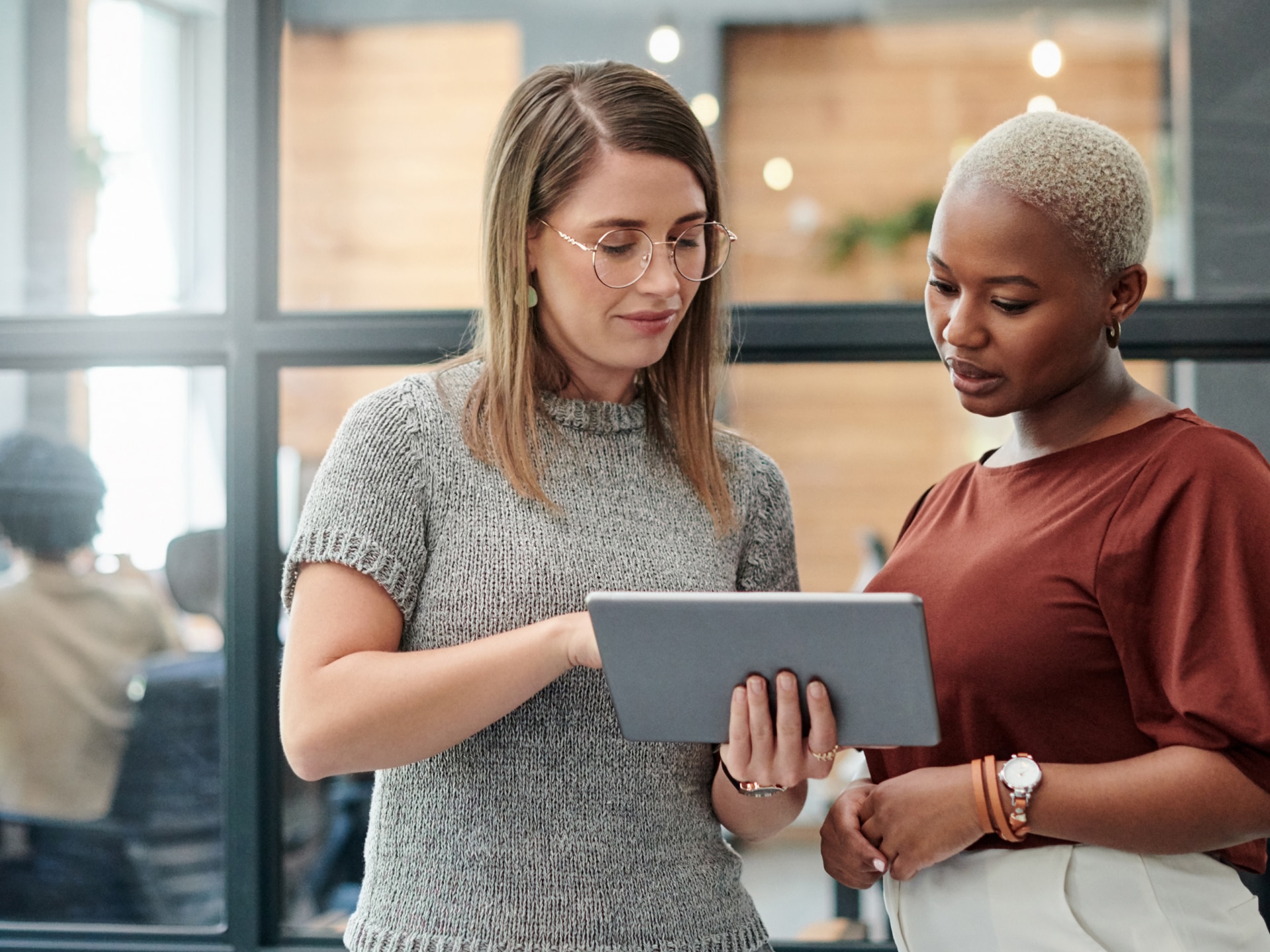 A Woman Dressed in Professional Business Clothes Showing Another Professionally Dressed Woman her iPad