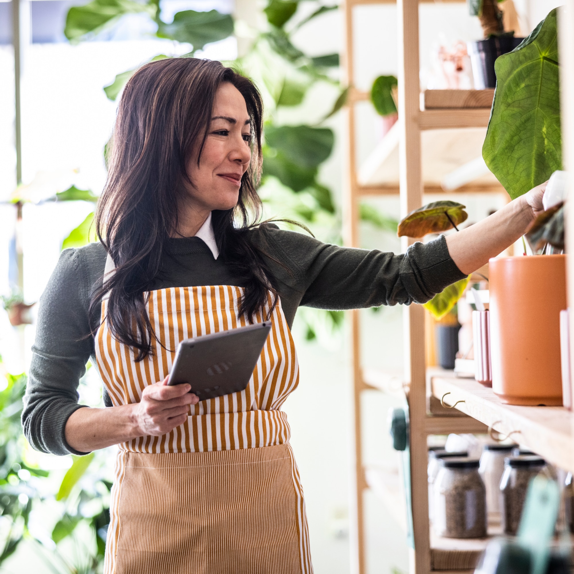 A Woman in her Plant Shop Organizing the Shelves as Light Steams in Through the Store Windows