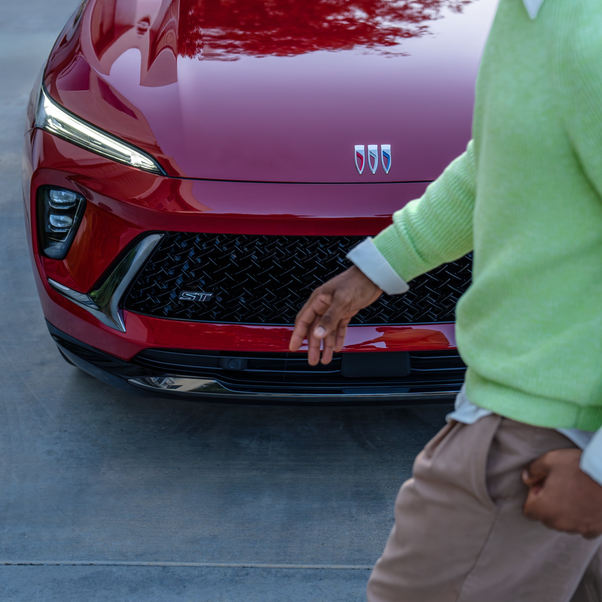 Close-up Front View of a Red Buick Vehicle with Distinct LED Headlights and Grille as a Person Walks Past