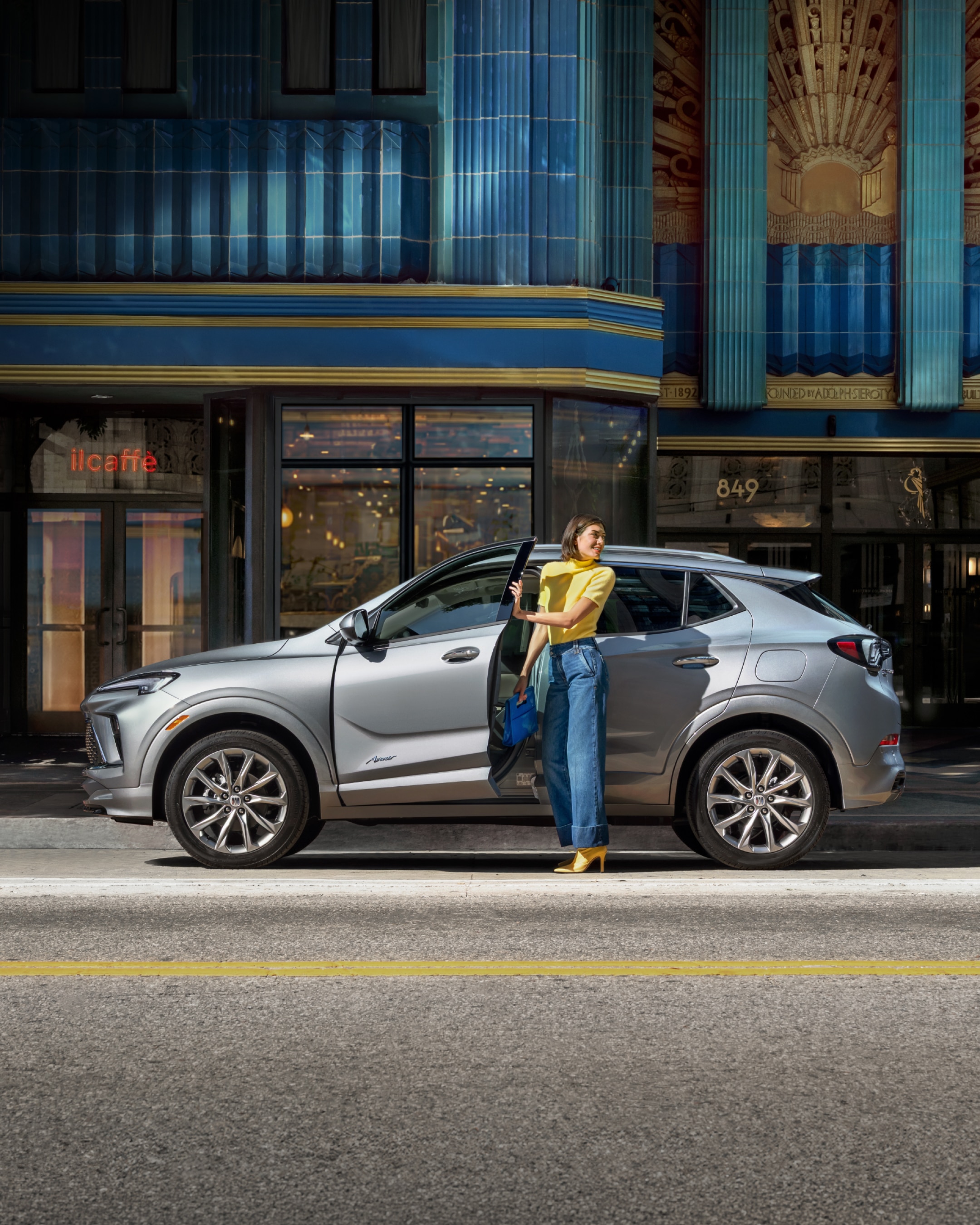 A Woman Standing by a Gray Buick Encore GX SUV on a City Street
