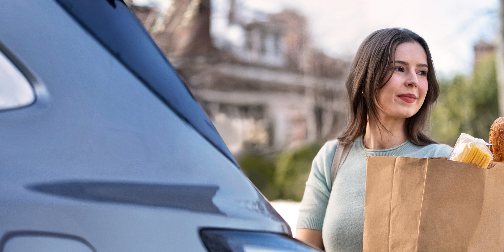 A Woman Holding a Bag of Groceries Behind a Vehicle