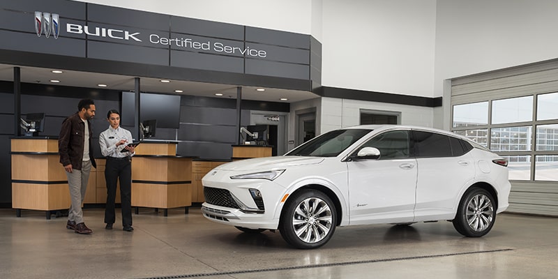 A Dealer Is Talking with a Customer While Holding a Tablet, with a White Buick Vehicle in Front of Them