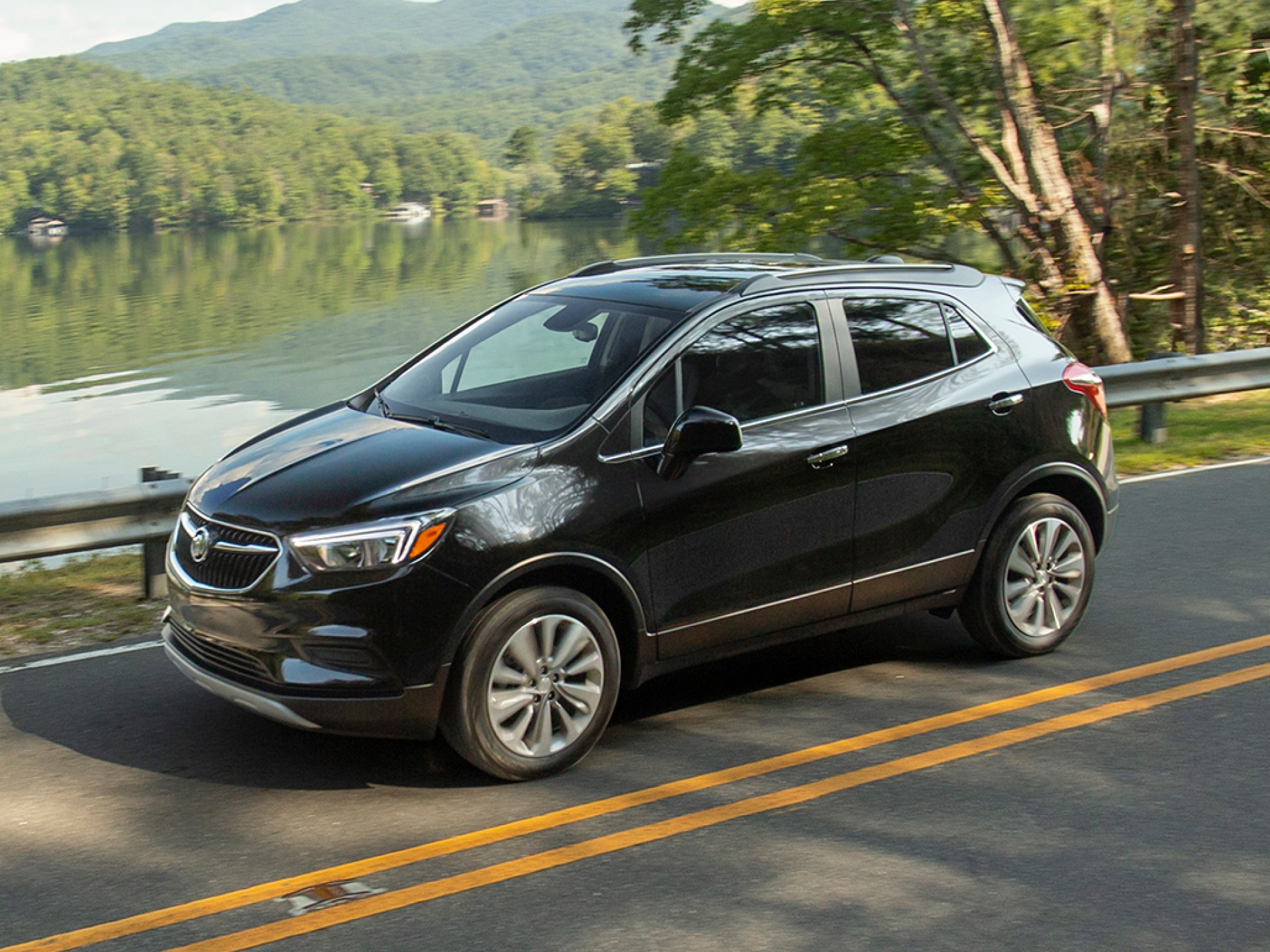 A Black Buick Encore Driving on a Road Next to a Lake with Lush Green Trees