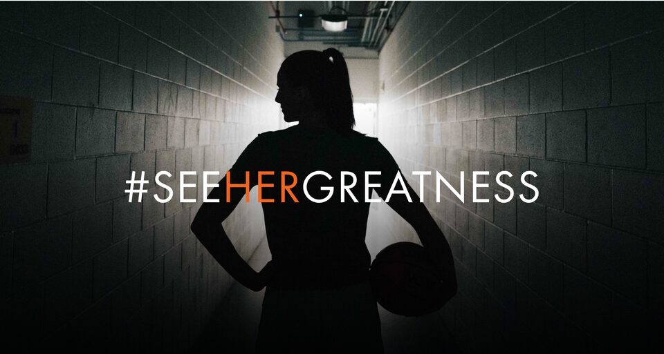 A Woman Basketball Player with her back to the shot in the tunnel with text Overlay saying "#Seehergreatness"
