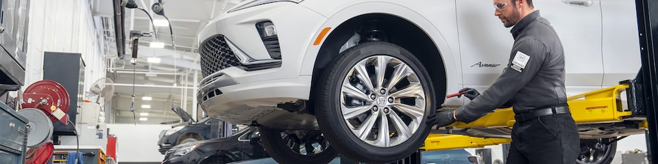 A Male Technician Inspecting a White Vehicle’s Tire While It’s Suspended in the  Air