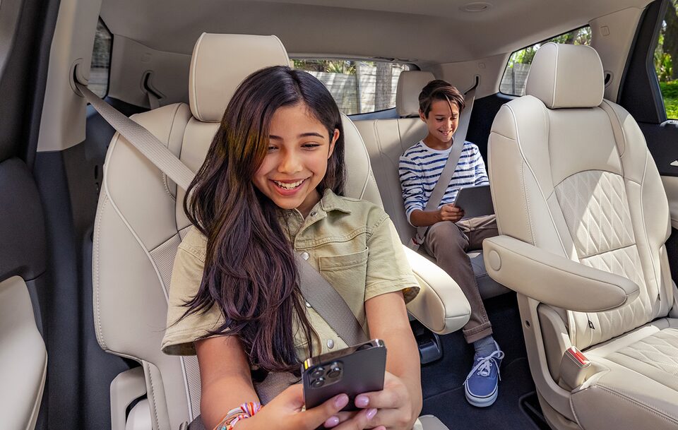 A Young Girl Holding a Smartphone and Boy Holding a Tablet in the back of a Buick