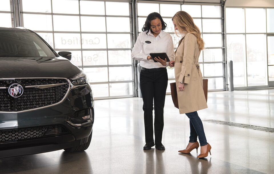 A Women and a Sales Rep Looking at a Tablet next to a Buick