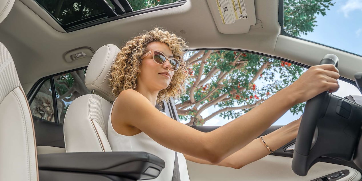 A Stylish Woman with Curly Hair Drives a Buick SUV with the Sunroof Open on a Sunny Day