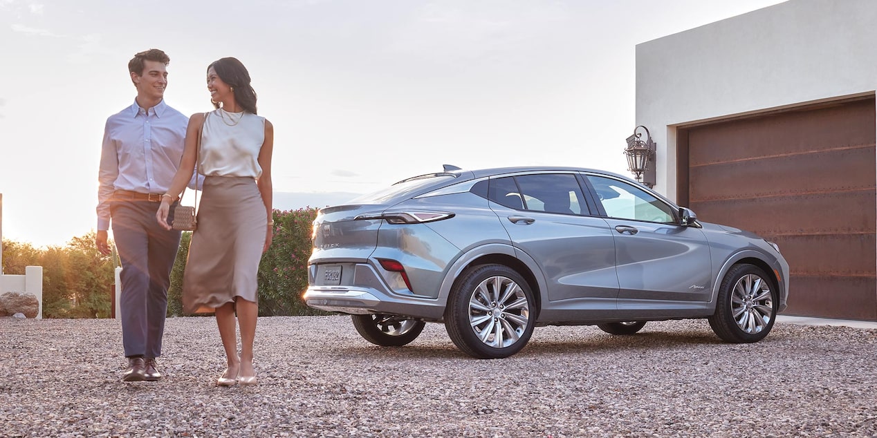A Gray Buick Envision Avenir Parked on a Gravel Driveway with a Smiling Couple Walking Beside It a Modern House in the Background
