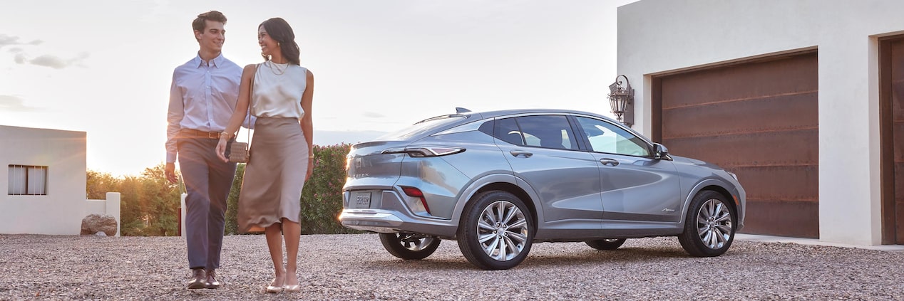 A Gray Buick Envision Avenir Parked on a Gravel Driveway with a Smiling Couple Walking Beside It a Modern House in the Background