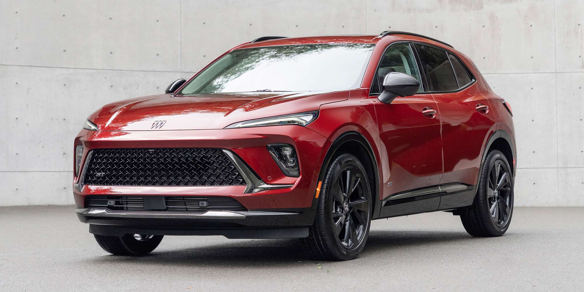 A Deep Red Buick Envista ST Parked on a Dark Gray Surface in Front of a Textured Concrete Wall 