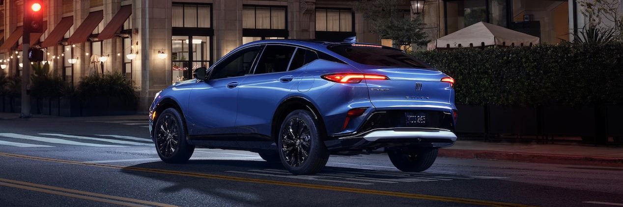 A Blue Buick SUV Parked on a City Street at Night with Taillights Illuminated and the Buick Logo Visible