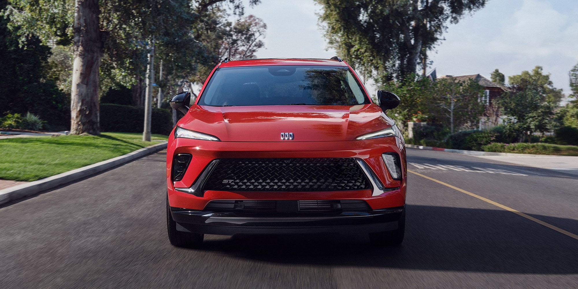 A Red Buick Envision Driving on a Shady Street With Trees on Both Sides