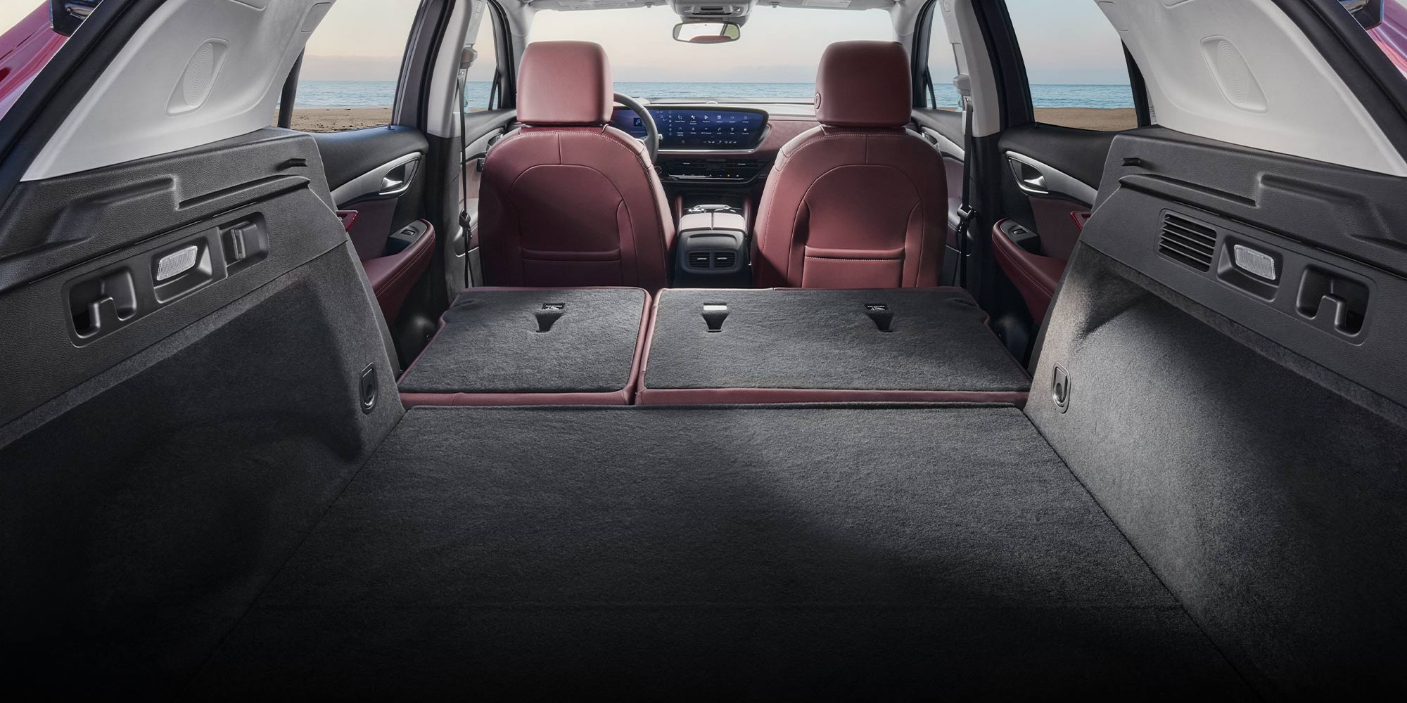 The Cargo Area of a 2026 Buick Envision Showing Flat-Folded Rear Seats and Red Front Seats With the Ocean in the Background