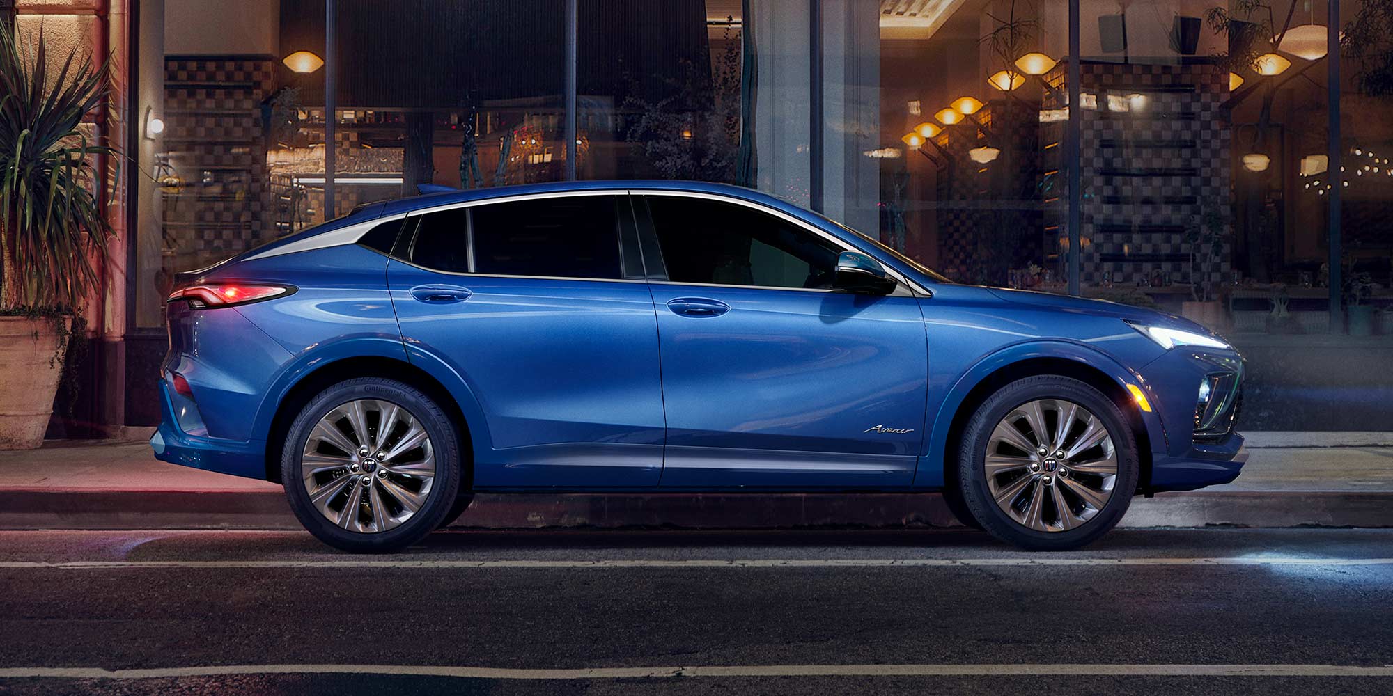 A Blue Buick Envista Parked at Night in Front of a Building with Lit Windows