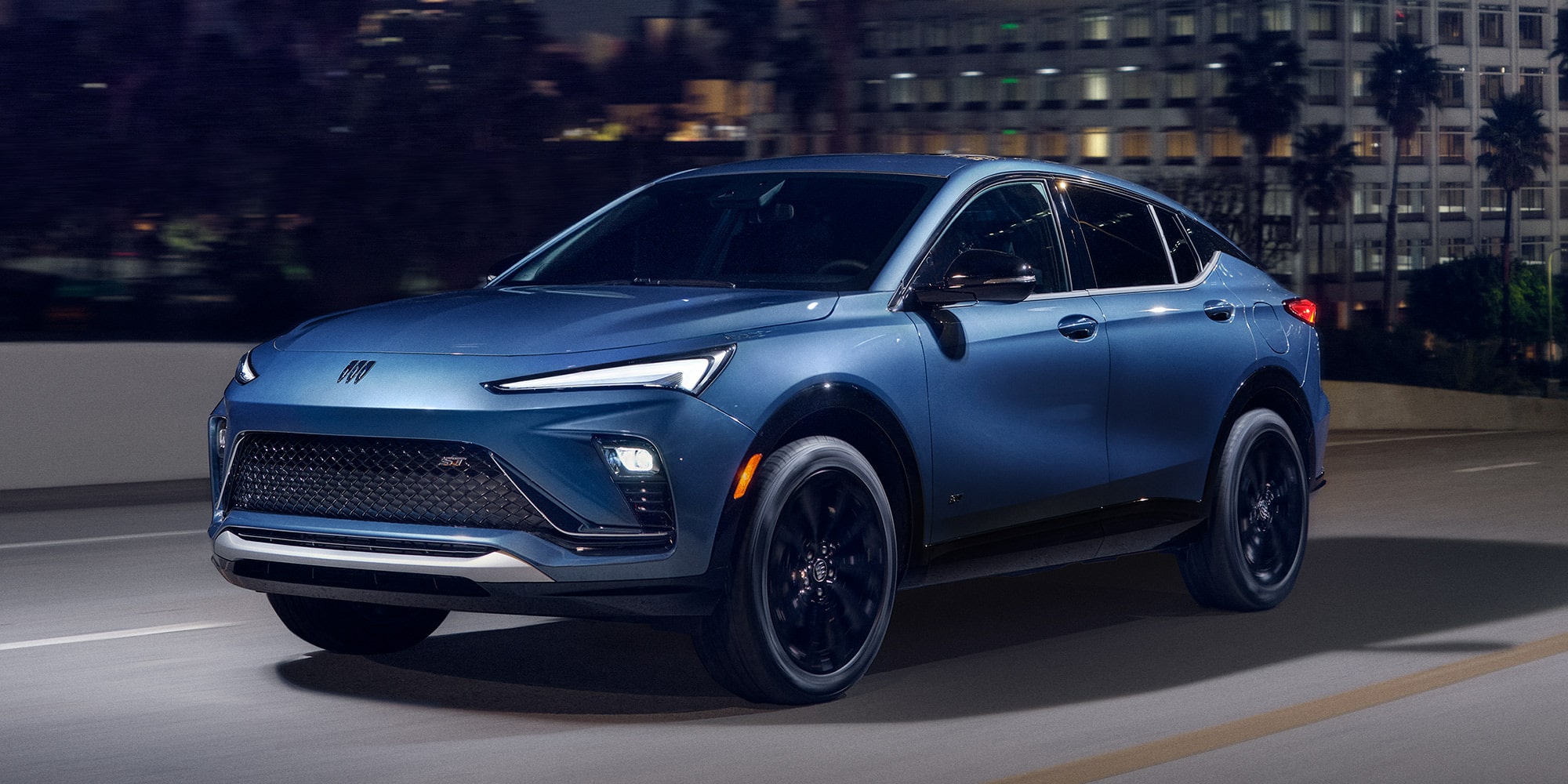 A Blue Buick SUV Driving on a City Street at Night with Illuminated Buildings in the Background