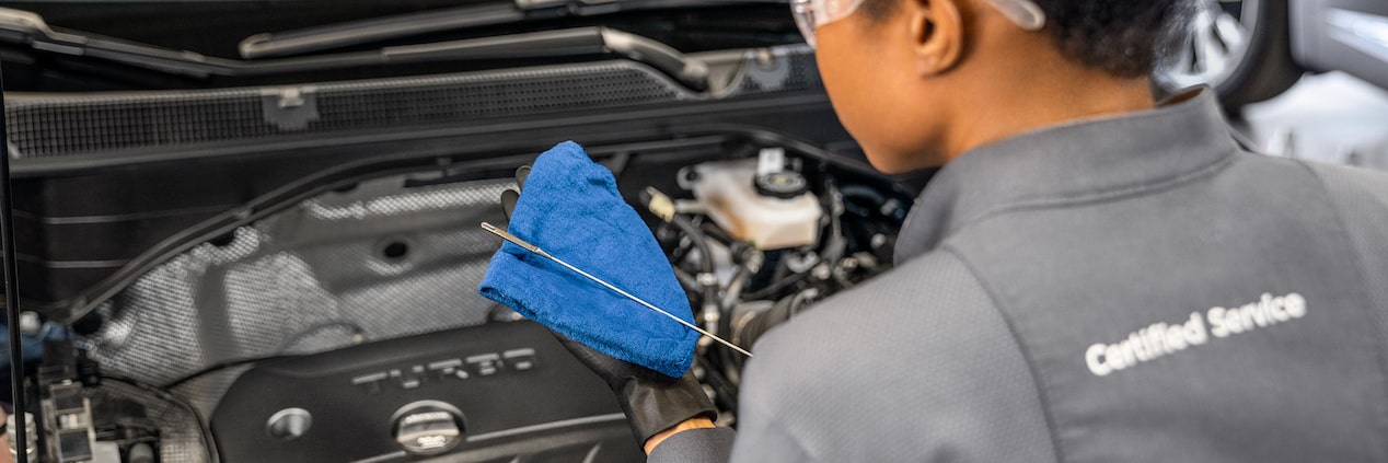 A Technician in Safety Glasses Checks the Oil in a Buick Engine with a Blue Cloth and Dipstick