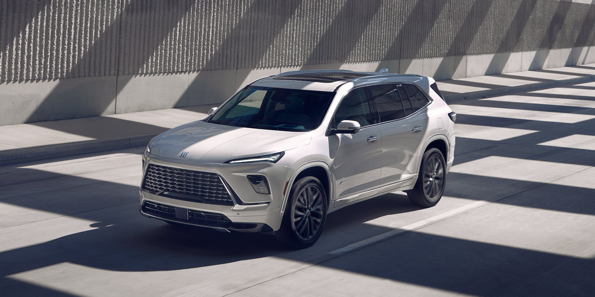 A Light Gray Buick Enclave Driving on an Urban Road Next to a Concrete Wall