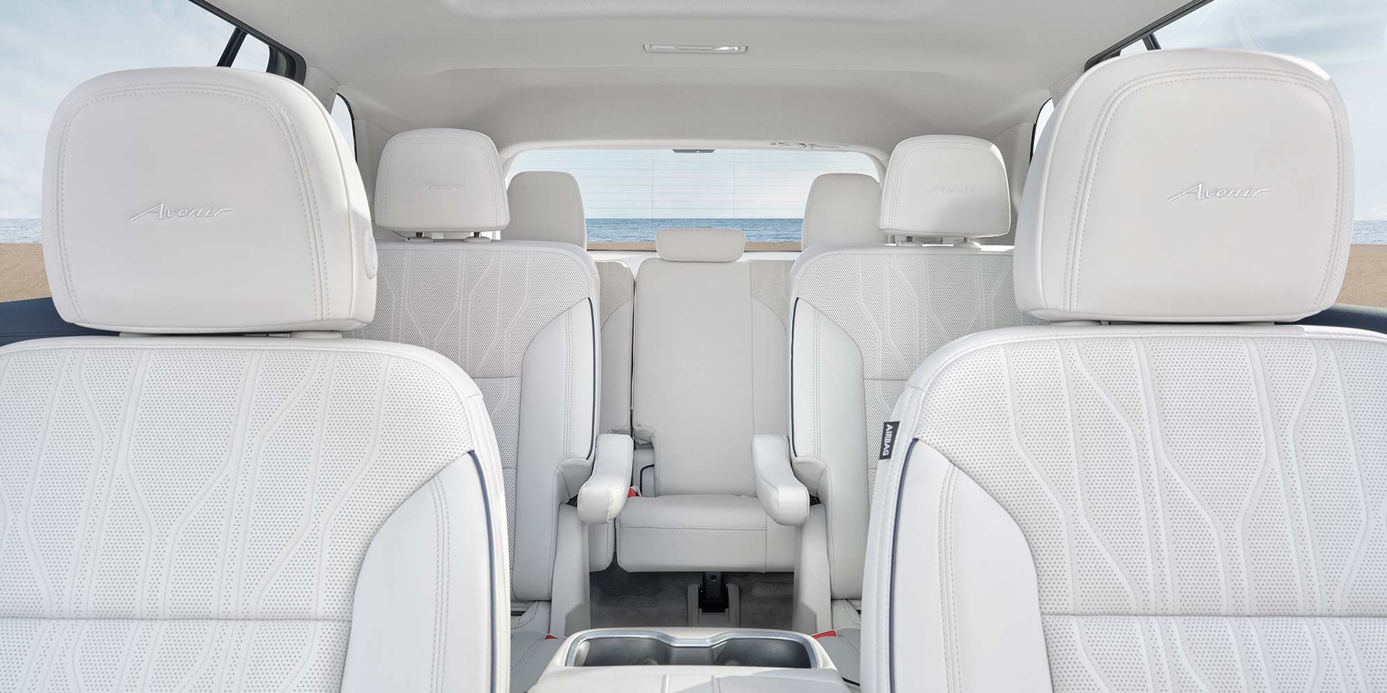 The Luxurious White Interior of a Buick Avenir SUV Showing All Three Rows of Seating with the Ocean in the Background