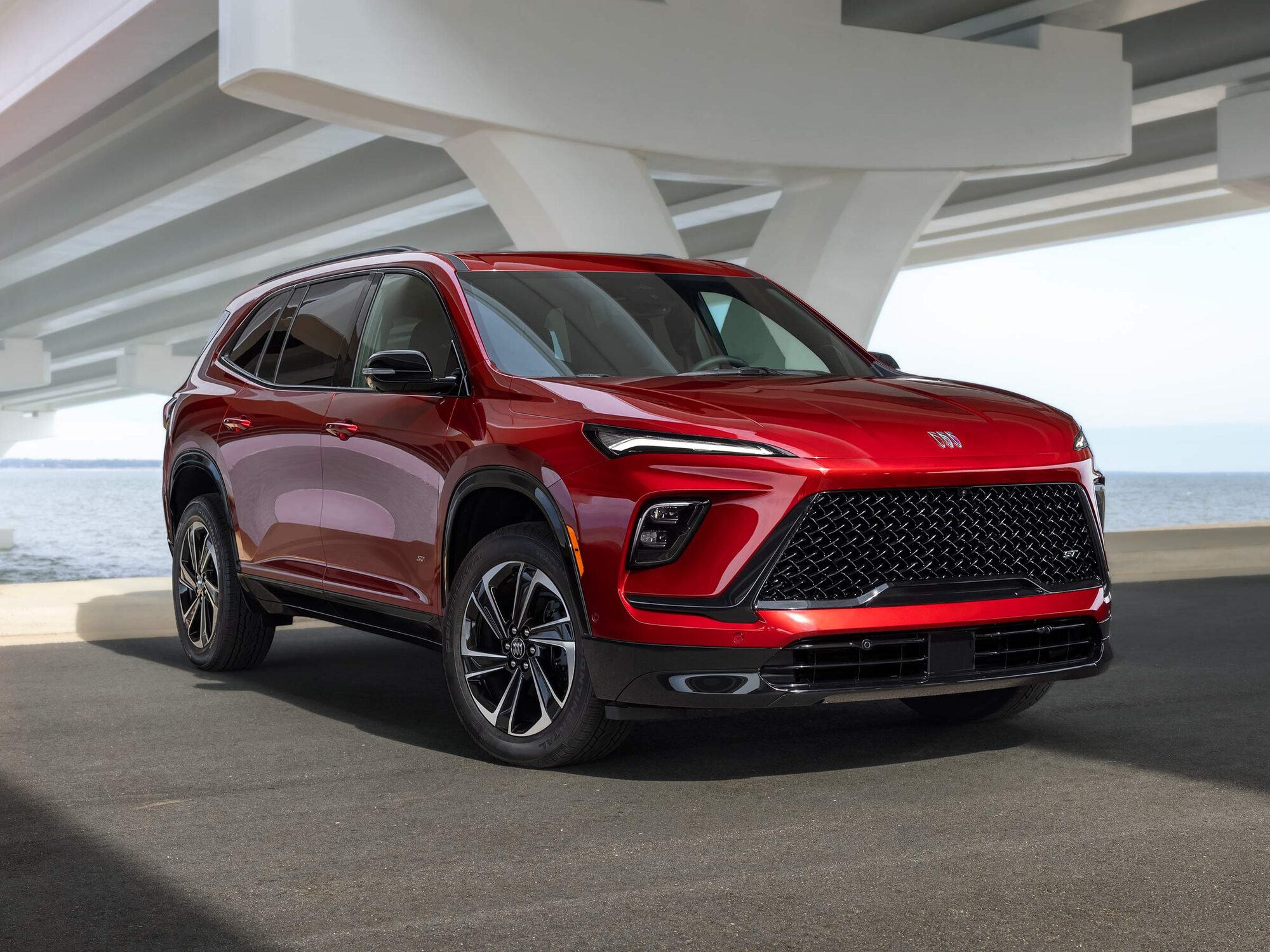 A Vibrant Red Buick Enclave SUV Parked Under a Concrete Bridge Next to the Water