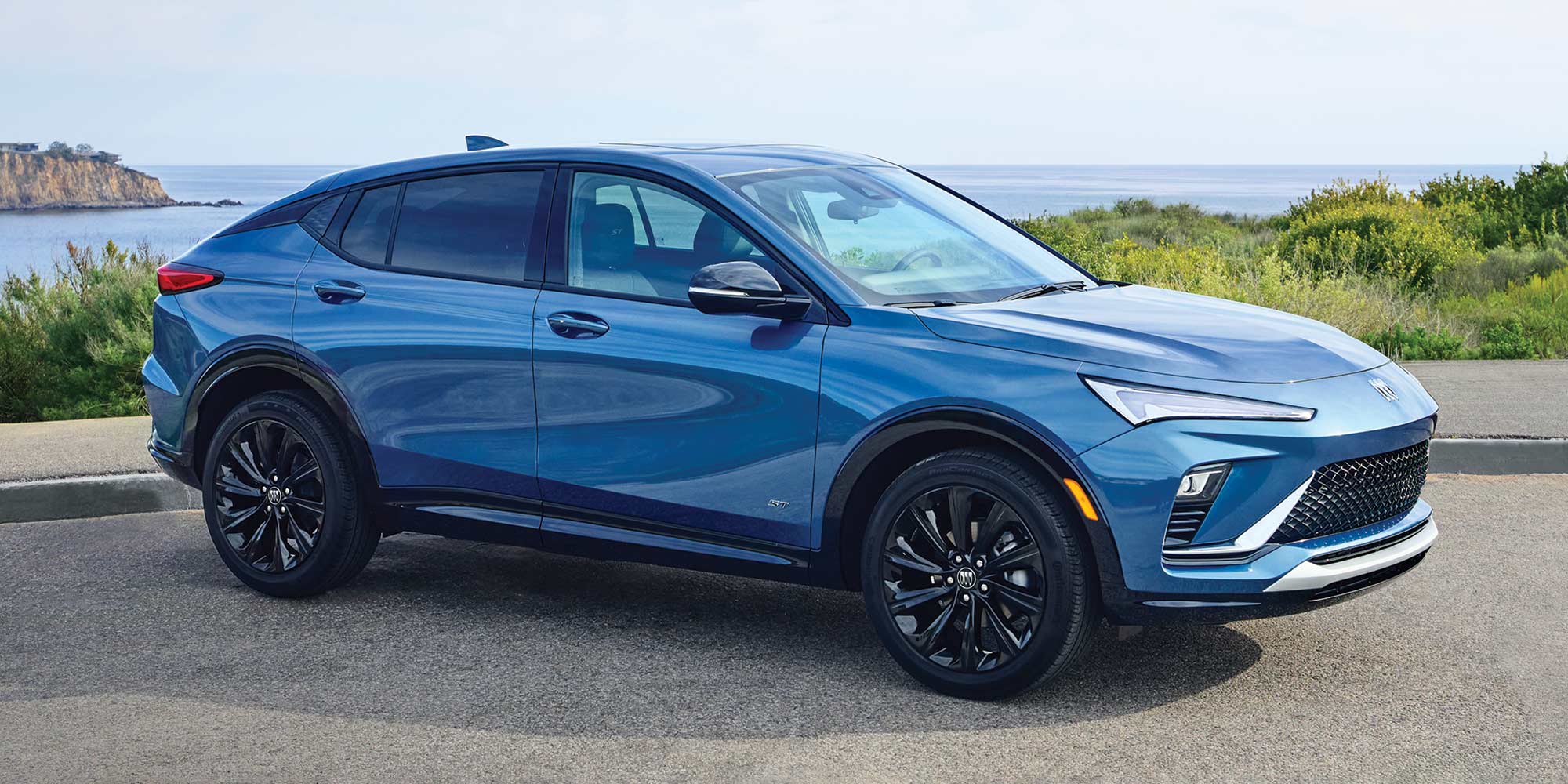 A Blue Buick Envista SUV Parked on a Coastal Road with the Ocean and Horizon in the Background
